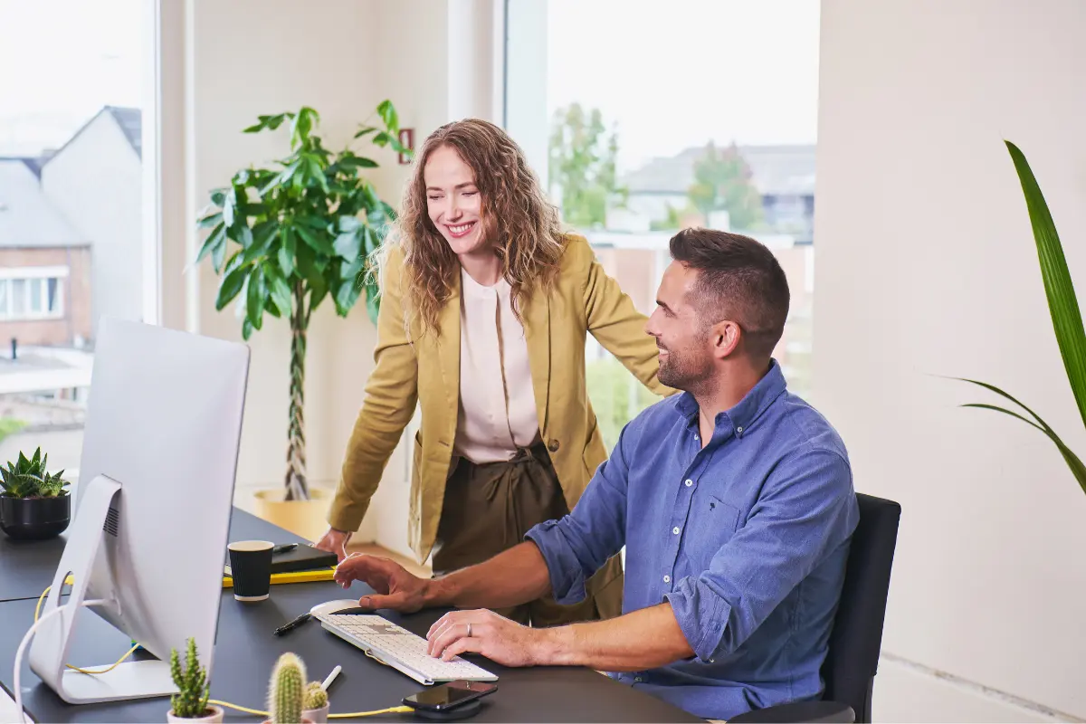 Zwei begeisterte Kolleg:innen an einem Schreibtisch mit Computer. Symbolbild für die Auswahl des passenden Tools zur Personaleinsatzplanung